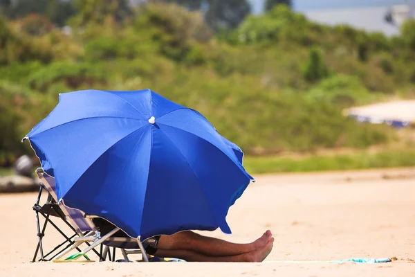 Mann entspannt sich am Strand unter blauem Sonnenschirm — Stockfoto