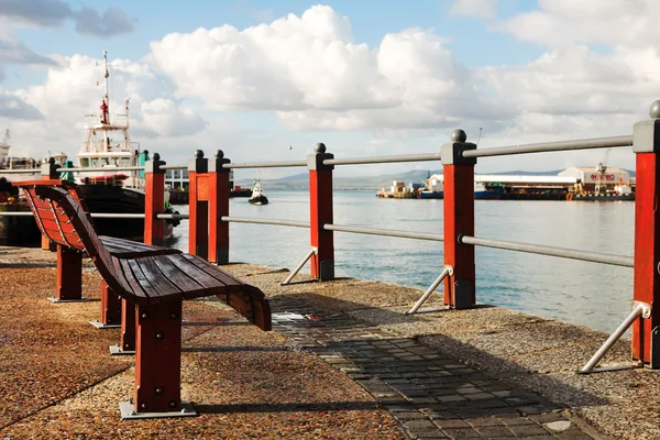 Dois assentos vermelhos no porto Waterfront da Cidade do Cabo, na África do Sul, com barcos no fundo em um dia nublado . — Fotografia de Stock