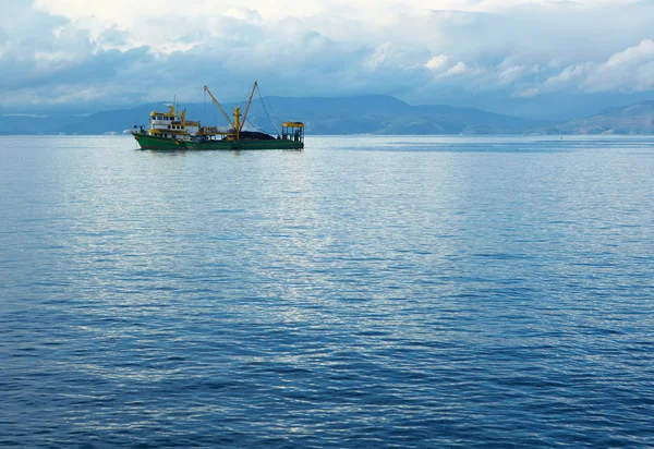 Jeden mały łowienie ryb trawler opuszczeniu portu w błękitne wody Morza Egejskiego do połowów na pochmurny zimowy dzień. — Zdjęcie stockowe