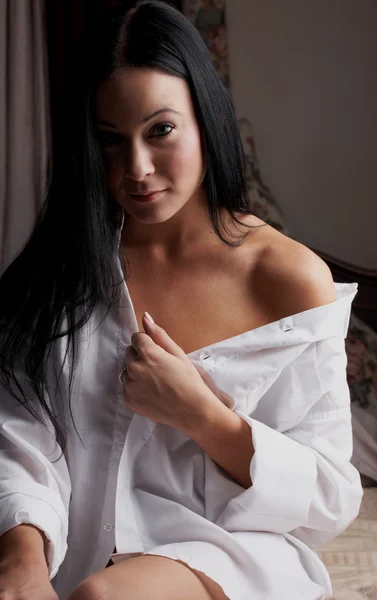 Young brunette caucasian woman wearing a white man's shirt sitting in her bedroom — Stock Photo, Image