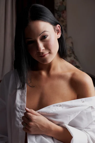 Young brunette caucasian woman wearing a white man's shirt sitting in her bedroom — Stock Photo, Image