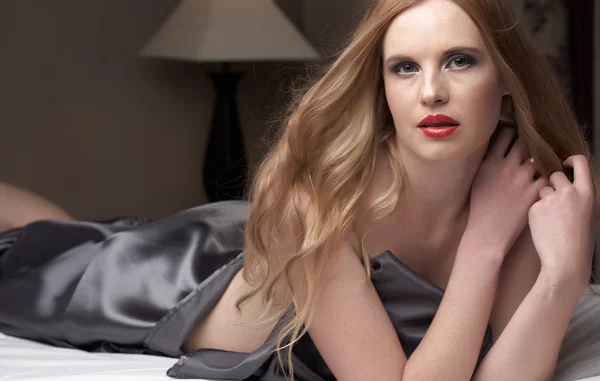 Sexy mujer adulta caucásica joven desnuda con labios rojos y cabello rubio acostado en una cama — Foto de Stock