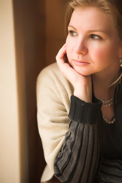 冬の初めに自然光ウィンドウの横に座っている金髪白人成人女性. — ストック写真