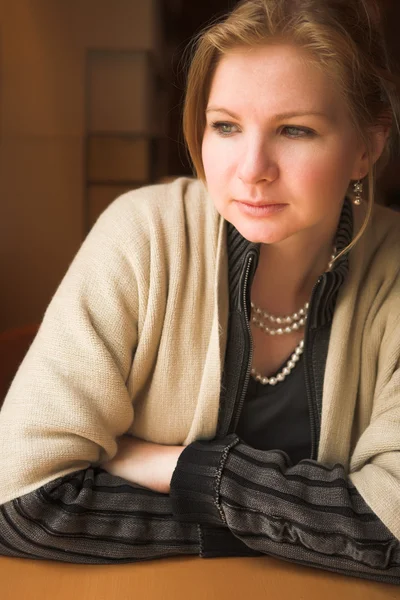 Blonde kaukasische erwachsene Frau sitzt im beginnenden Winter neben einem Fenster mit natürlichem Licht. — Stockfoto