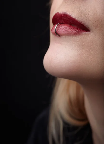 Durchbohrte rote Lippen einer jungen erwachsenen kaukasischen Frau vor dunklem Hintergrund. — Stockfoto