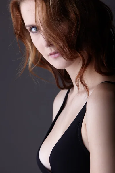 Giovane donna rossa adulta caucasica con occhi verdi e pelle molto chiara in lingerie nera su uno sfondo grigio neutro — Foto Stock
