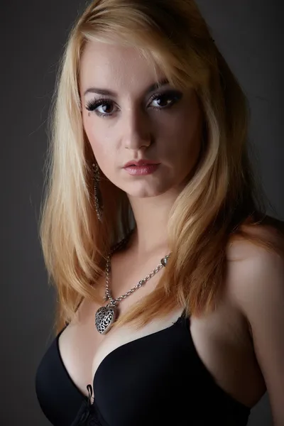 Young adult caucasian woman with blonde hair and prominent jewelry on a neutral grey background with black lingerie and big brown eyes — Stock Photo, Image