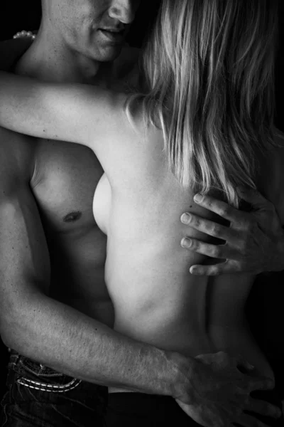 Joven y en forma pareja adulta caucásica en un abrazo. Semi-desnuda y en topless sobre un fondo oscuro. Blanco y negro  . — Foto de Stock