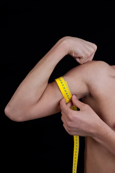 Ung man mäta sin arm med centimeter — Stockfoto