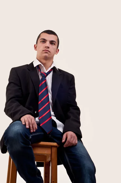 Серьезный молодой человек, сидящий на стуле на цветном фоне — стоковое фото