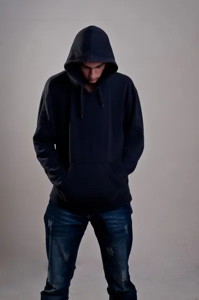 Teenager with hoodie looking down against a dirty gray wall — Stock Photo, Image