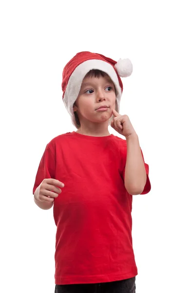 Retrato de belo menino no chapéu de Papai Noel com o dedo na bochecha isolado no fundo branco — Fotografia de Stock