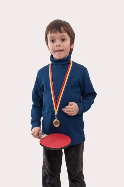 Niño pequeño con medalla de oro en el cuello y raqueta de tenis de mesa en la mano — Foto de Stock