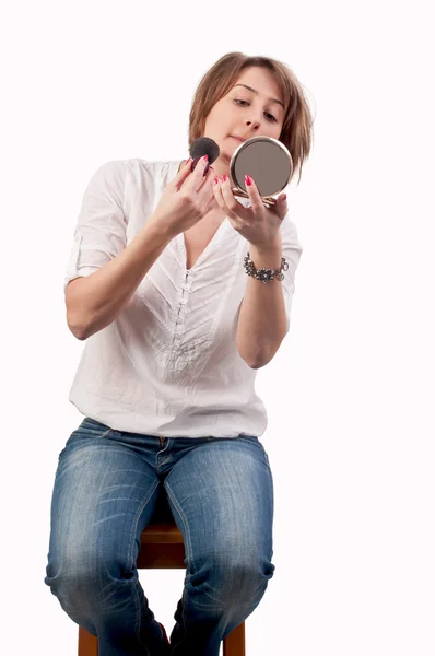 Приваблива молода жінка дивиться у дзеркало і наносить рум'яна — стокове фото