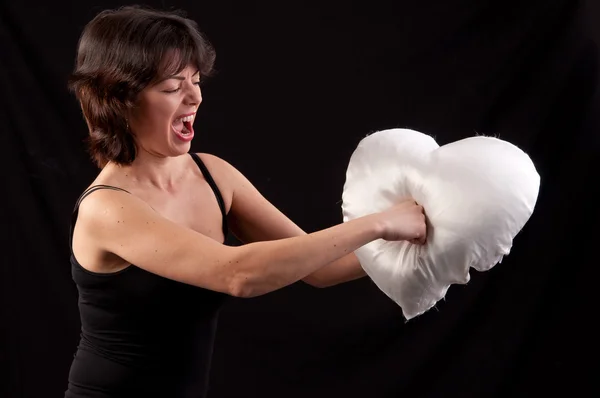 Angry woman strikes with fury a heart-shaped pillow on black bac — Stock Photo, Image
