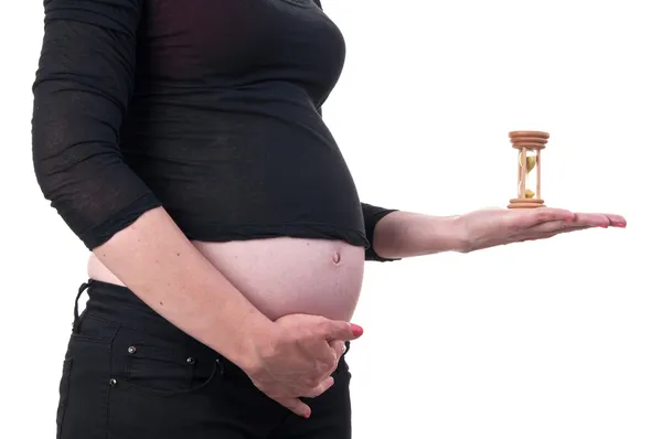 Immagine di una giovane donna incinta con una clessidra accanto — Foto Stock