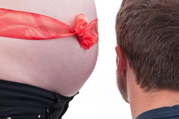 Glücklicher Vater, der dem schwangeren Bauch seiner Frau mit roter Schleife zuhört — Stockfoto