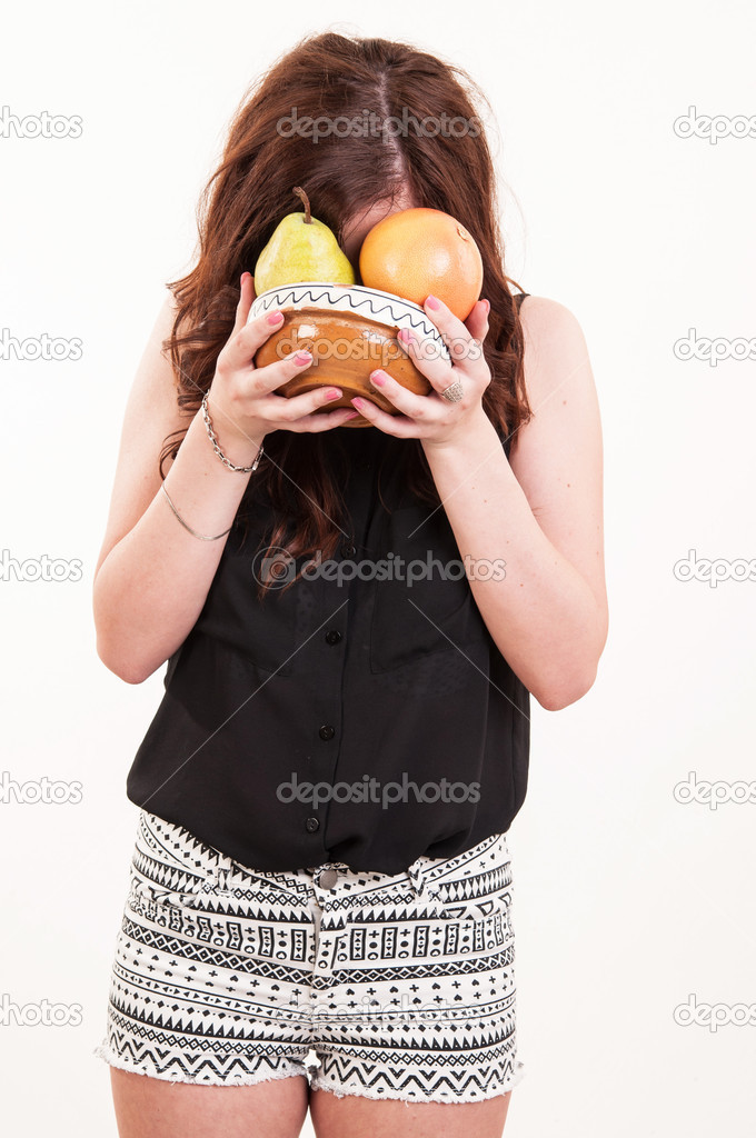 Young fit woman with her face in a bowl with fruits, funny conce
