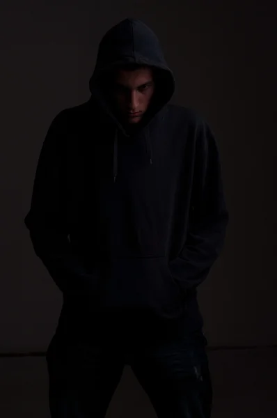 Adolescente con sudadera con capucha mirando hacia abajo contra una pared gris oscuro sucio — Foto de Stock