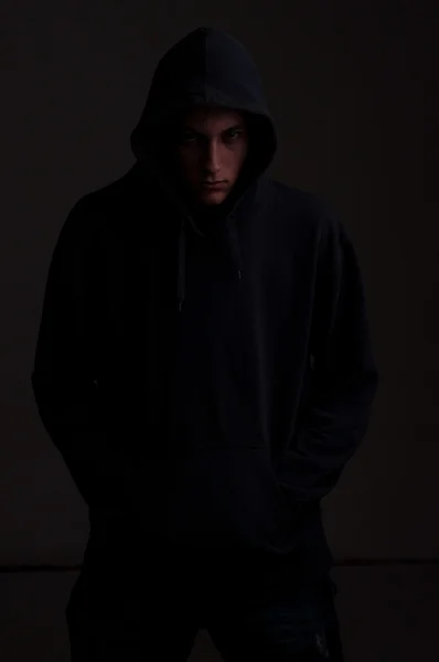 Teenager with hoodie looking down against a dirty black wall — Stock Photo, Image