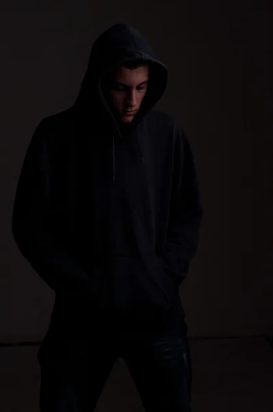 Teenager with hoodie looking down against a dirty black wall — Stock Photo, Image