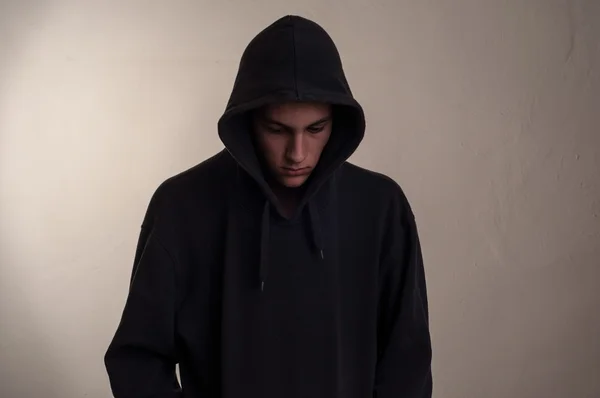 Teenager with hoodie looking down against a dirty gray wall — Stock Photo, Image