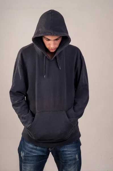 Tiener met hoodie kijkt neer tegen een vuile grijze muur — Stockfoto