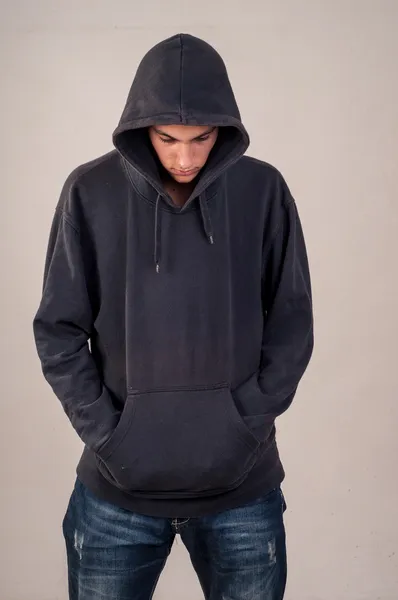 Έφηβος με hoodie κοιτάζοντας προς τα κάτω σε ένα βρώμικο τοίχο γκρι Royalty Free Εικόνες Αρχείου