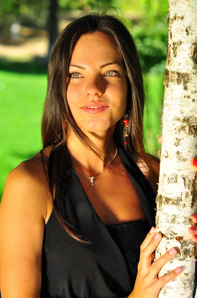 Beautiful young woman posing near the green tree on nature — Stock Photo, Image