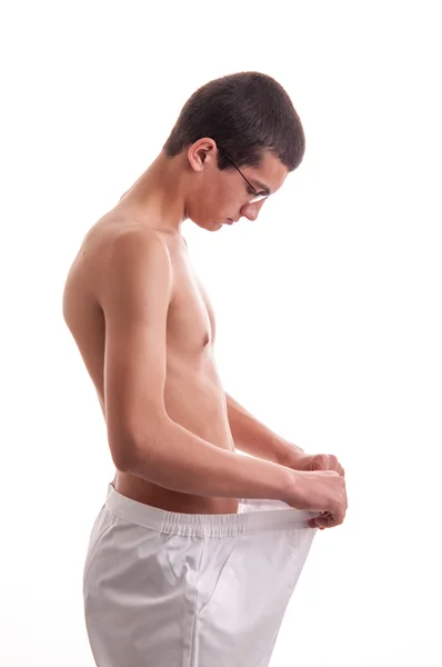 Young man showing his lost weight by putting on an old pants — Stock Photo, Image