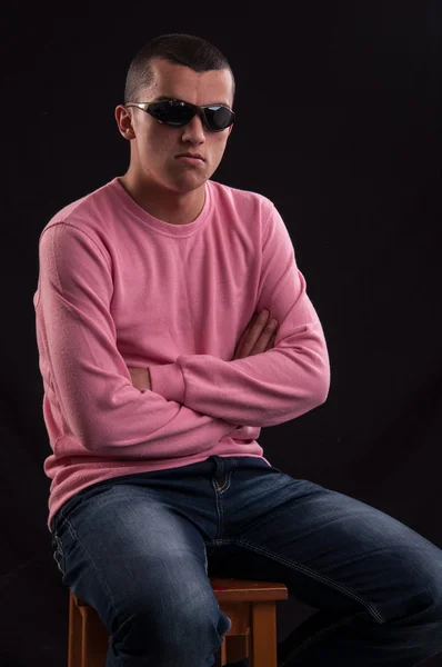 Allvarlig unga kaukasiska man med solglasögon sitter på stol — Stockfoto