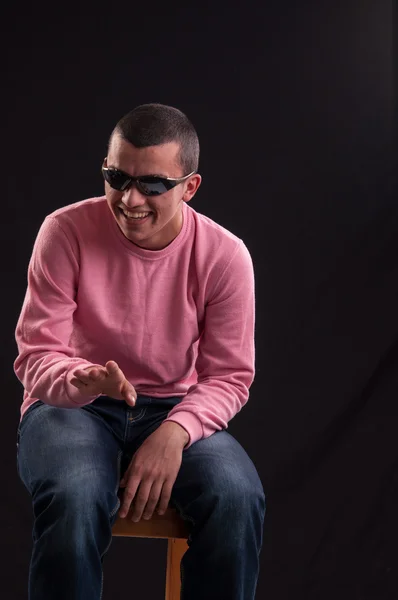 Young man with sunglasses sitting on chair and laughing — Stock Photo, Image