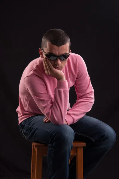 Молодой кавказский мужчина в солнечных очках сидит на стуле — стоковое фото