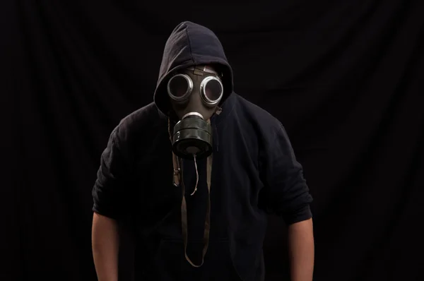 Man in black clothes wearing a classic gas mask over a dark back — Stock Photo, Image