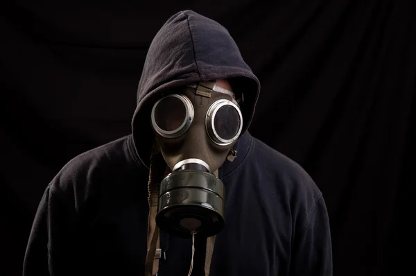 Man in black clothes wearing a classic gas mask over a dark back — Stock Photo, Image