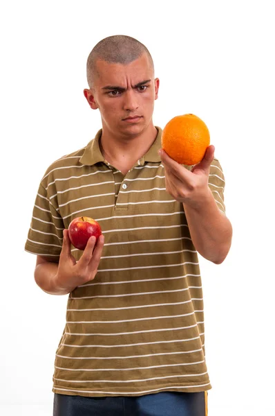 Jovem comparando laranja com maçã vermelha — Fotografia de Stock