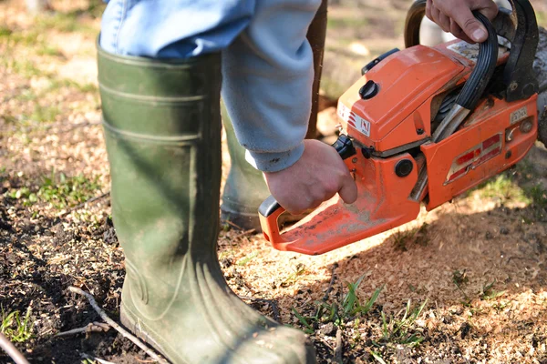 Een man is met behulp van een oranje kettingzaag te snijden boomtakken liggend op — Stockfoto
