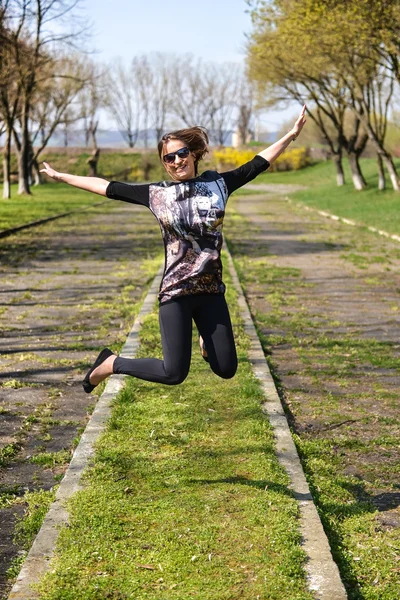 Bardzo młoda kobieta, skoki na zielonej trawie i uśmiechnięta pełna jo — Zdjęcie stockowe