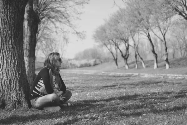 Miło brunetka siedzący pod drzewem w parku (czarny i wh — Zdjęcie stockowe