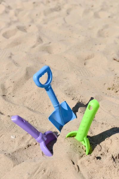 Blue, green and purple beach shovel stuck in the sand on a sunny — Stock Photo, Image