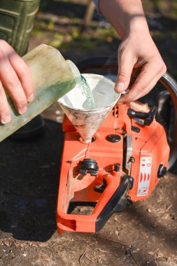 Hand refilling the chainsaw with fuel clipart