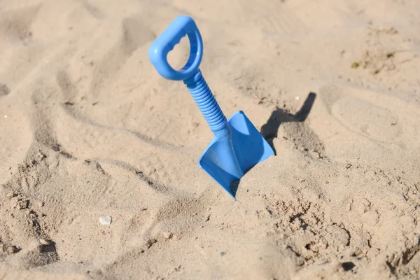 Blue beach shovel stuck in the sand by a child — Stock Photo, Image