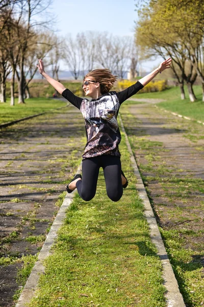 緑の芝生の上でジャンプとジョーの完全な笑みを浮かべてはかなり若い女性 — ストック写真