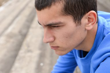 Merdivenlerde oturan ve kameraya bakarak genç çocuk