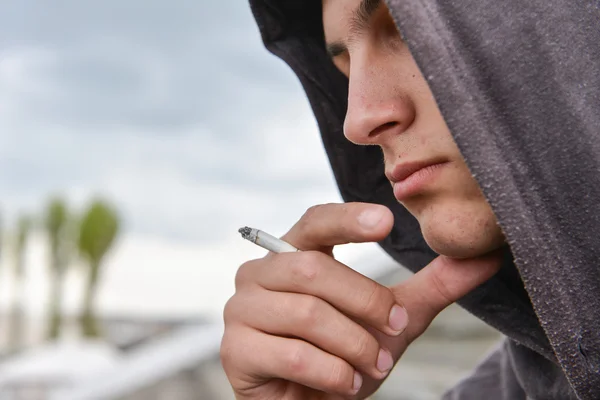 Menino adolescente pensativo e preocupado com capuz preto é fumar cigarro — Fotografia de Stock