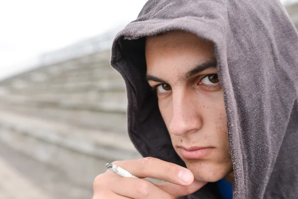 Adolescente con sudadera con capucha negra está fumando cigarrillos al aire libre. Mira. — Foto de Stock