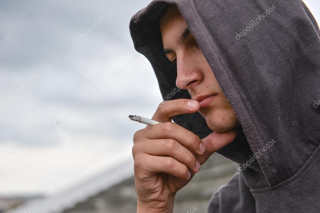 pensive and worried teenage boy with black hoodie is smoking cig