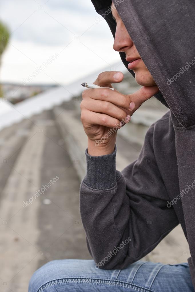 pensive and worried teenage boy with black hoodie is smoking cig