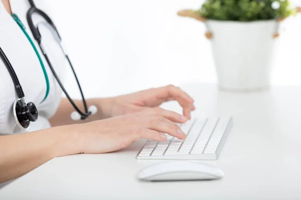 Doktor masasında bilgisayarda yazıyor.