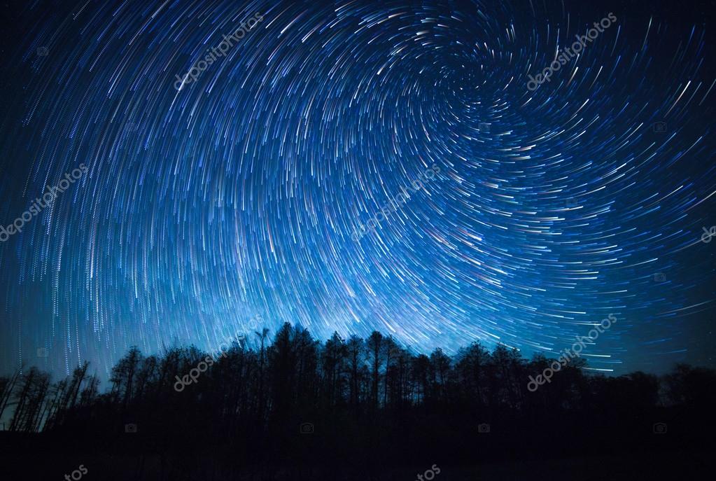 Cielo nocturno, senderos de estrellas espirales y el bosque fotografía